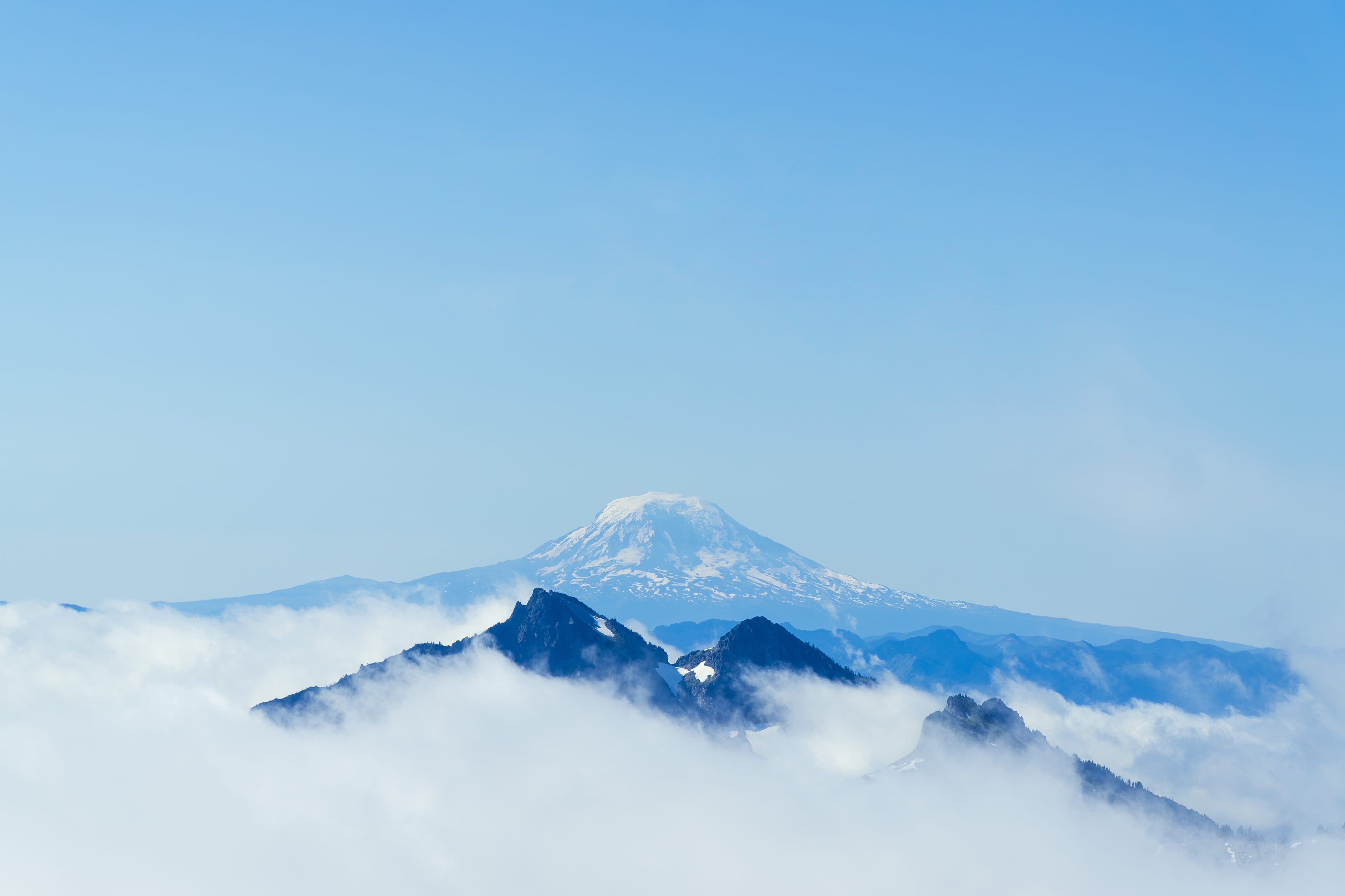 A snow-capped mountain rising above a sea of clouds under a clear blue sky
