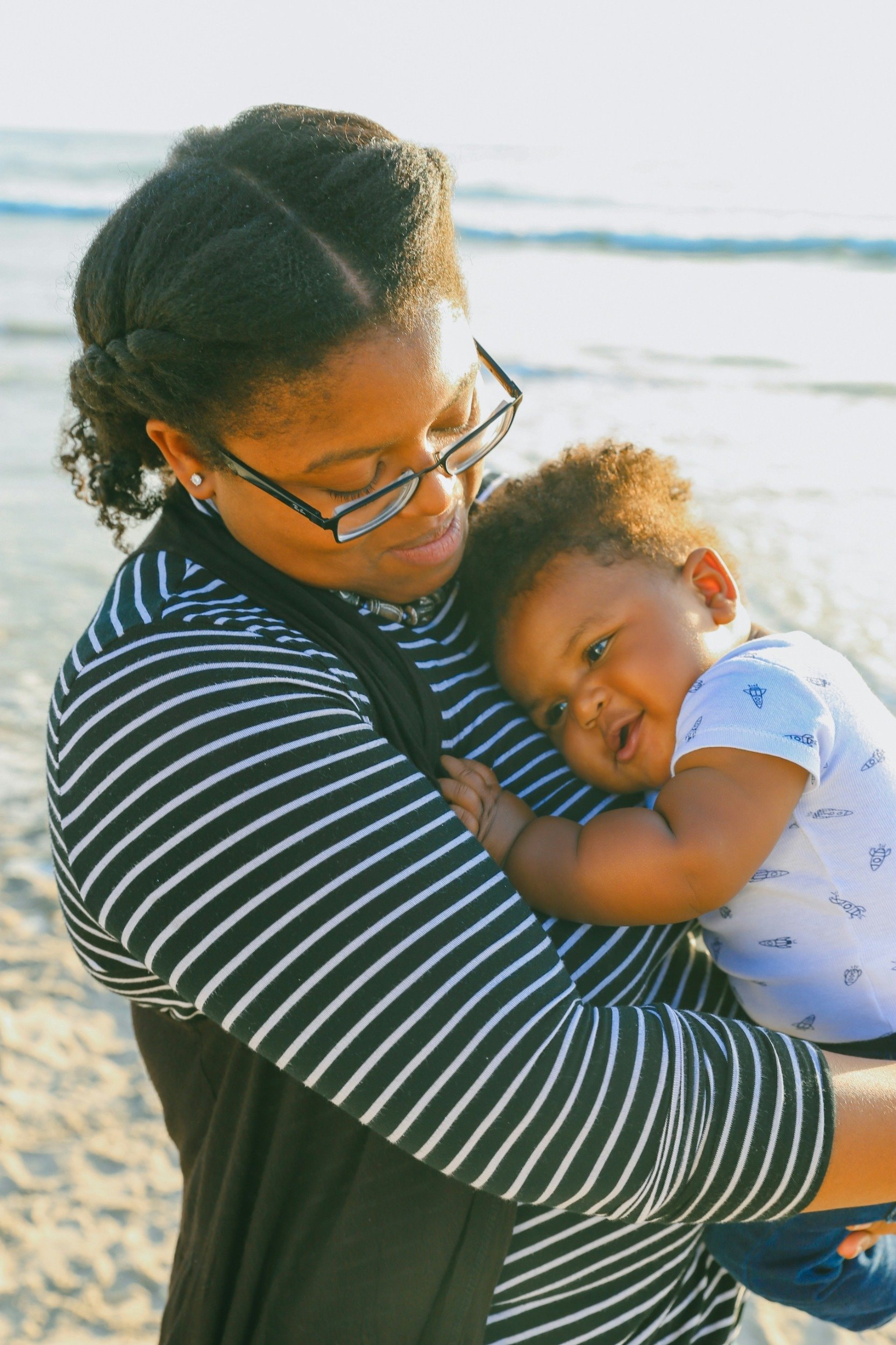 A mother holding her baby on a beach.